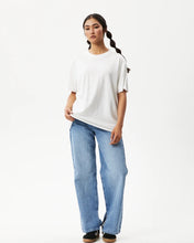 Load image into Gallery viewer, Afends Women&#39;s Slay Oversized Tee in White on a model posing with one hand on her hip in front of a white background
