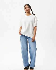 Afends Women's Slay Oversized Tee in White on a model posing with one hand on her hip in front of a white background