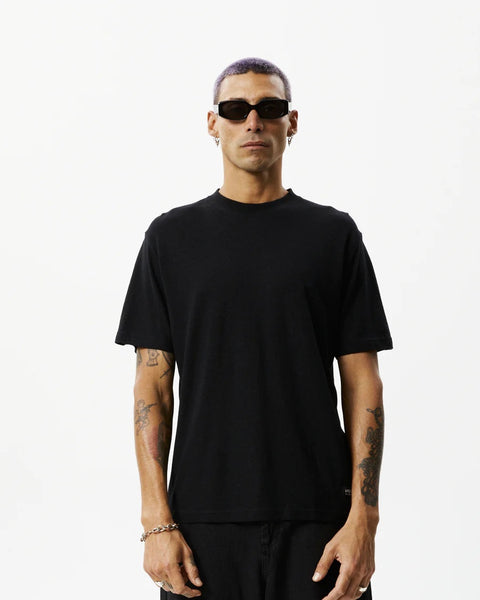 the Afends Men's Classic Hemp Retro Tee in Black on a model posing in front of a white background staring into the camera