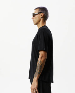 side view of the Afends Men's Classic Hemp Retro Tee in Black on a model posing in front of a white background