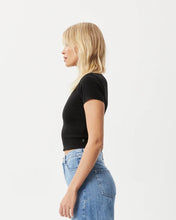 Load image into Gallery viewer, side view of the the Afends Women&#39;s Iconic Rib Tee in Black on a model posing in front of a white background
