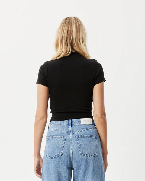back view of the the Afends Women's Iconic Rib Tee in Black on a model posing in front of a white background