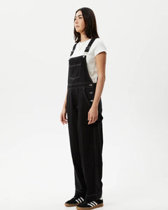 side angled view of the the Afends Women's Louis Overalls in Washed Black on a model standing against a white background