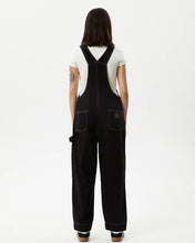 Load image into Gallery viewer, back view of the the Afends Women&#39;s Louis Overalls in Washed Black on a model standing against a white background
