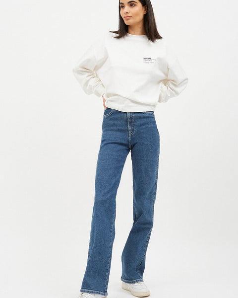 the Dr. Denim Women's Moxy Jean in Cape on a model posing in front of a neutral background with her hands on her hips looking off to the side