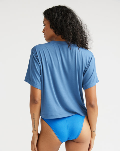 back view of model wearing the Richer Poorer Women's Night Knit Tee in Blue Horizon paired with blue briefs standing with her head looking toward her left shoulder