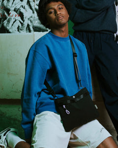 the Taikan Sukhoi Cross Body Bag in Black worn cross body by a model posing on his knees