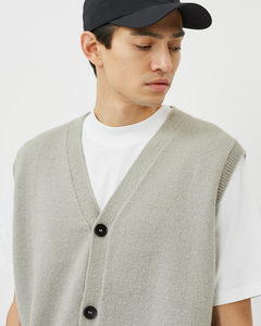 Close up view of the Minimum Men's Vastar Vest in Ghost Grey layered over a white tee on a model wearing a black cap looking over his shoulder