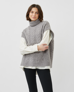 Model standing with crossed arms wearing the Minimum Women's Cablina Sweater Vest in Gull over a white long sleeve tee