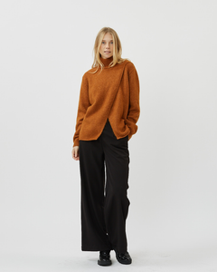 front view of a model standing wearing the Minimum Women's Meline Sweater in Roasted Pecan paired with wide leg black pants and shiny black shoes