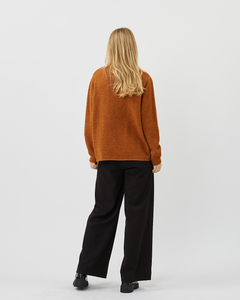 back view of the Minimum Women's Meline Sweater in Roasted Pecan worn by a model standing paired with black wide leg pants