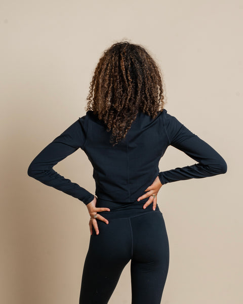back view of the Girlfriend Collective ReSet Long Sleeve Tee in Black on a model posing with her hands on her hips