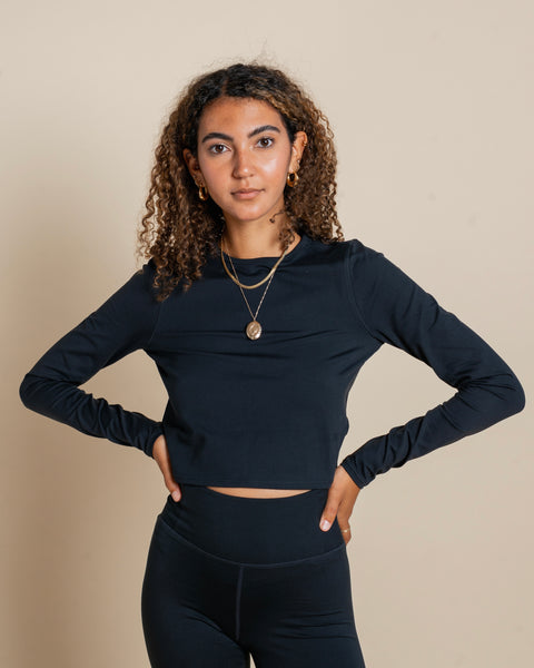 the Girlfriend Collective ReSet Long Sleeve Tee in Black worn by a model posing with her hands on her hips