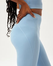 Load image into Gallery viewer, close up side view of model posing with her hands on her hips wearing the Girlfriend Collective High-Rise Crop Legging in Cerulean
