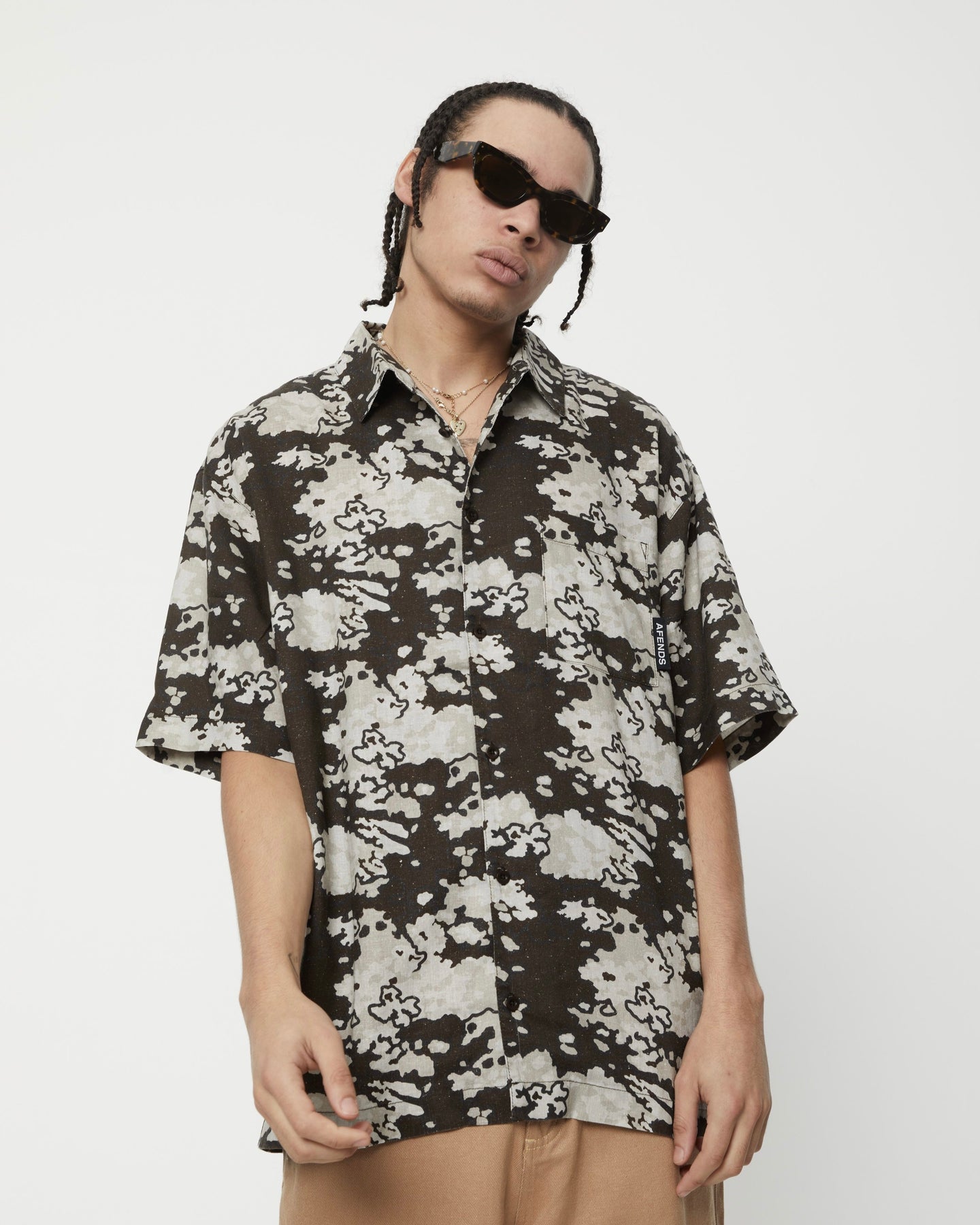 the Afends Men's Short Sleeve Jungle Shirt in Earth Camo on a model posing with his head tilted to one side