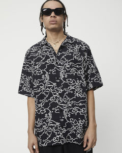 a close up of the Afends Men's Script Short Sleeve Cuban Shirt in Black Camo on a model