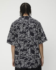 a close up of the back view of the Afends Men's Script Short Sleeve Cuban Shirt in Black Camo on a model