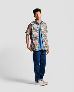 the Poplin & Co Men's Short Sleeve Printed Shirt in Hibiscus worn by a model standing against a neutral background on a slight angle with one hand in the back pocket of his jeans