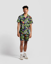 Load image into Gallery viewer, the Poplin &amp; Co Men&#39;s Camp Shirt in Tropical Birds worn by a model standing against a neutral background paired with matching shorts and sneakers
