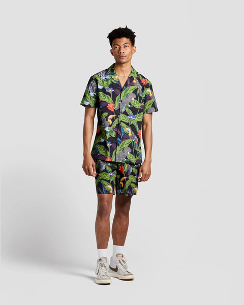 the Poplin & Co Men's Camp Shirt in Tropical Birds worn by a model standing against a neutral background paired with matching shorts and sneakers