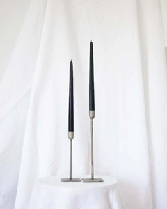 a pair of Socco Designs Taper Candles in black in two tapers of varying heights against a white sheet background