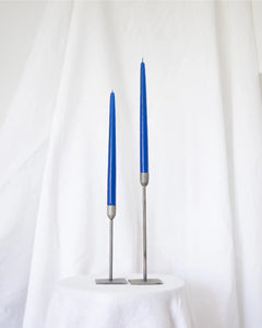 a pair of Socco Designs Taper Candles in bright blue in two tapers of varying heights against a white sheet background