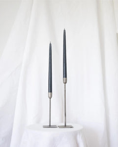 a pair of Socco Designs Taper Candles in charcoal in two tapers of varying heights against a white sheet background
