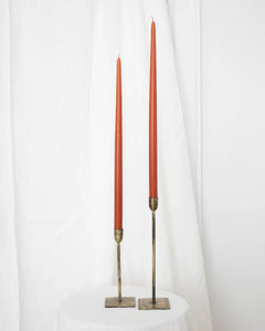 a pair of Socco Designs Taper Candles in terracotta in two tapers of varying heights against a white sheet background